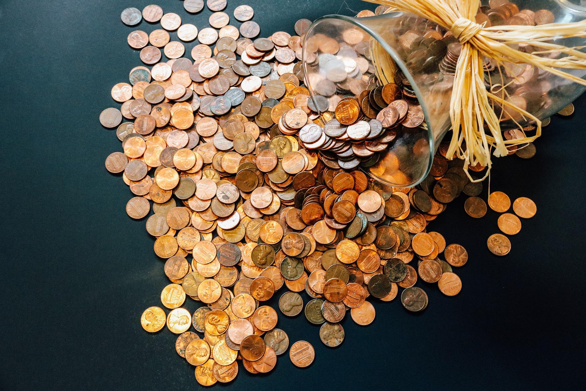 A pile of coins pouring out.of a vase with a straw ribbon