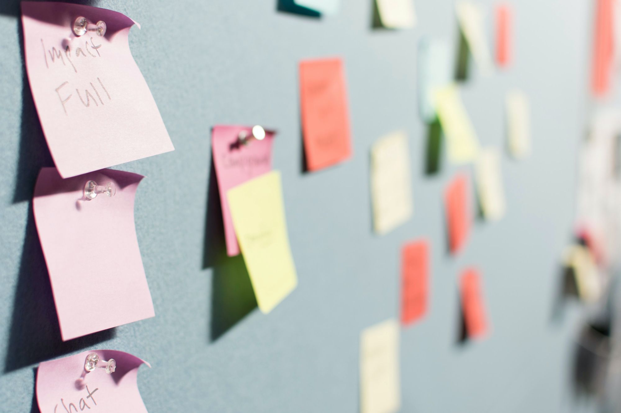 Various coloured post-its pinned on a blue grey board.