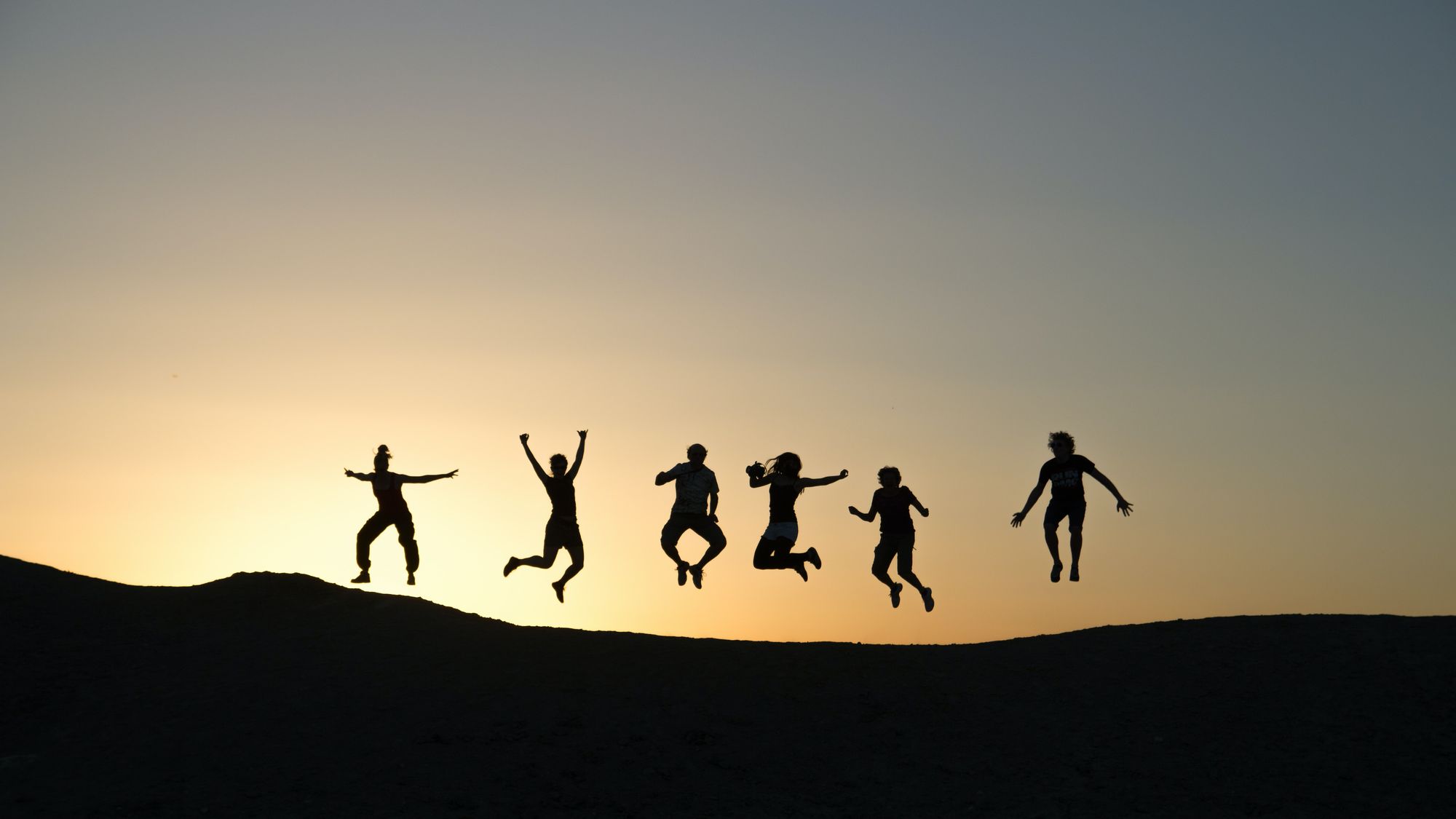 Silhouettes of 6 people jumping during sunset