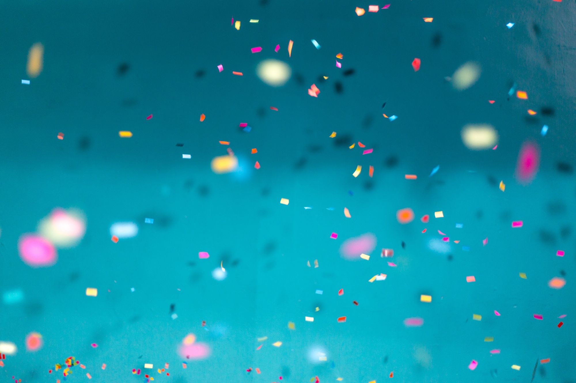 Colurful confetti falling down with a teal background.