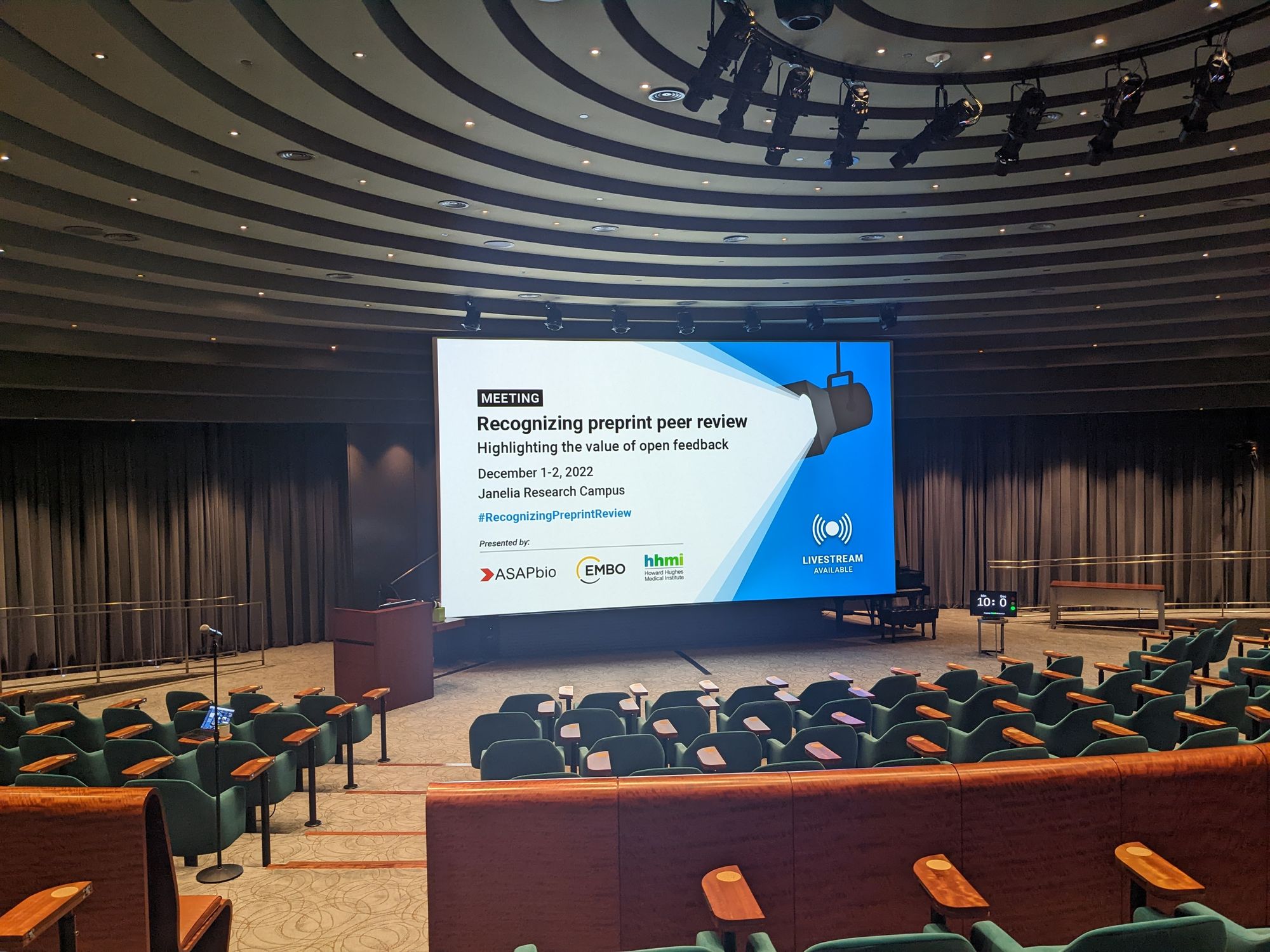 Empty auditorium with a slide showing the title, date, venue, and organizer of the meeting.