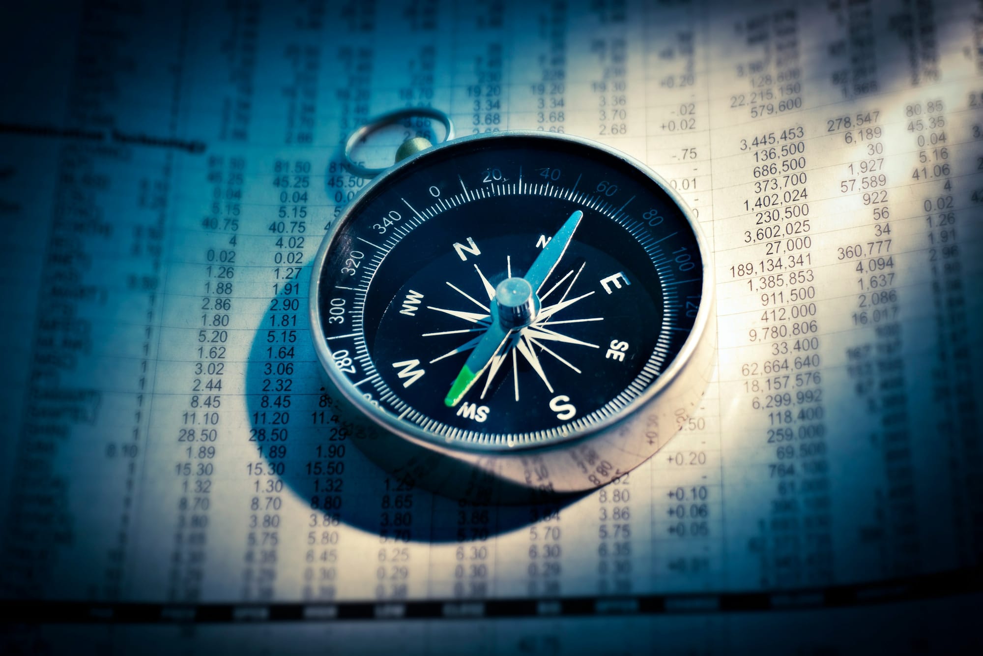 A compass sitting on a sheet of paper with columns of prices. 